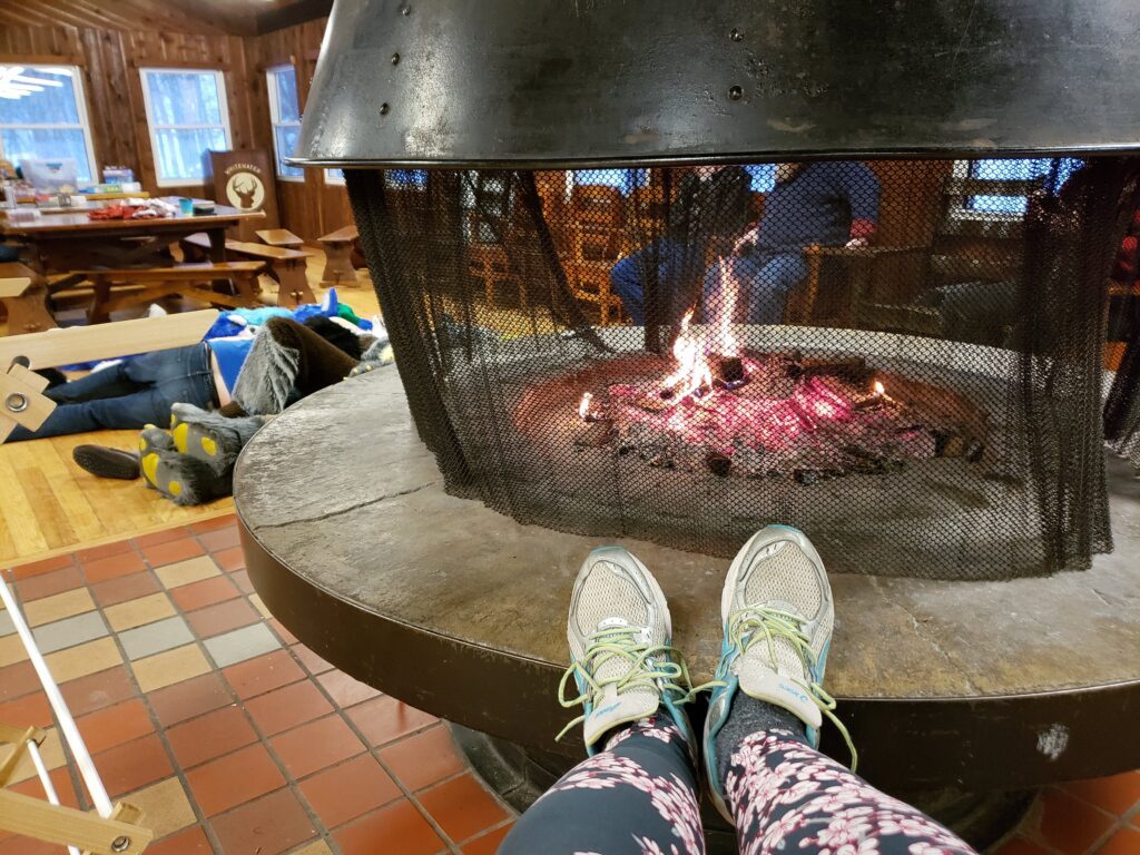 A camper enjoys keeping their feet warm near the fireplace